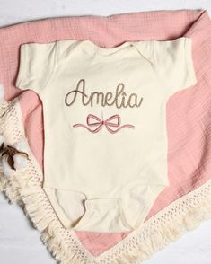 This personalized embroidered bodysuit makes a perfect baby shower, birthday, or any occasion gift for a baby!   Your baby shirt will be embroidered with the name or words of your choice (max of 10 characters), in the chainstitch script font shown in the photos. A pretty bow will be embroidered below. This item is made to order and is machine washable. See the photos for available shirt colors and size chart.  All colors of thread are available, I have too many to list!  If you would like a very Customizable Cotton Onesie For First Birthday, Cotton Short Sleeve Onesie For First Birthday, Cute Personalized Cotton Onesie, Cotton Baptism Onesie With Short Sleeves, Cotton Onesie For Baptism, First Birthday Cotton Romper In Cream, Pink Cotton Baptism Onesie, Personalized Cotton Onesie For Baptism, Pink Cotton Onesie For Gift