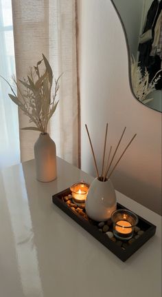 candles are lit on a tray in front of a mirror and vase filled with plants