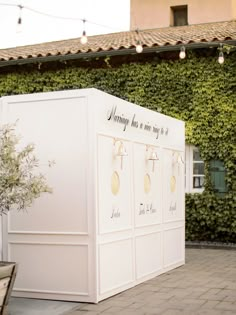 a small white box sitting on top of a brick floor next to a building covered in vines