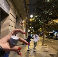 two people walking down the street at night with one person holding a cup in their hand