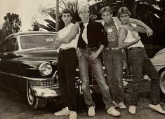 four young men posing in front of an old car