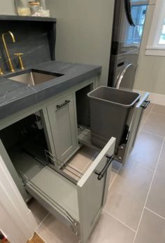 a kitchen with a sink, dishwasher and trash can in the middle of it