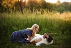 a woman is playing with her dog in the grass at sunset or sunrise, and she has long blonde hair on her head