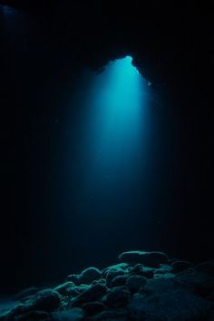 an underwater cave with light coming from the water's surface and rocks under it