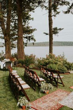 an outdoor ceremony set up with wooden chairs and rugs on the grass next to trees