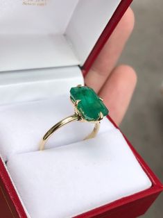 a person holding an emerald ring in a red box with the lid open to show it's inside