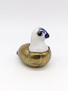 a small white and blue bird sitting on top of a golden object with black eyes