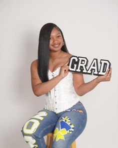 a woman sitting on top of a stool holding up a sign that says grad