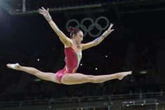 a woman in a red leotard doing a trick on the balance beam at an olympics event