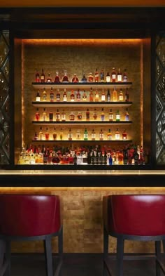 two red chairs sitting in front of a bar with bottles on the wall behind it