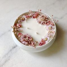 a white candle with pink flowers floating in it on a marble countertop next to a bowl