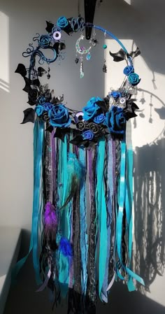 a blue and black dream catcher hanging from the ceiling with feathers, flowers and beads