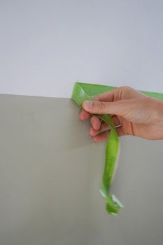 a hand is holding a green piece of paper on the wall and pulling it up