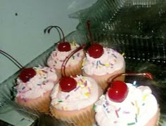 several cupcakes with white frosting and cherries on top are sitting in a plastic container