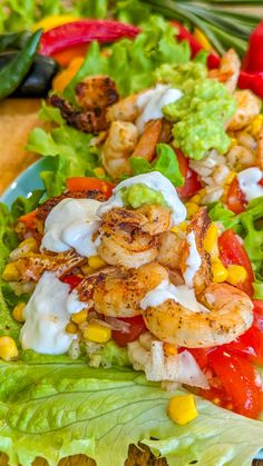 a salad with shrimp, lettuce and tomatoes on it sitting on a table