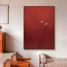 two birds flying in the sky on a red wall above a couch and table with chairs