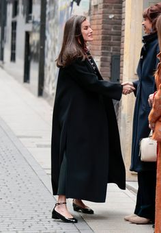 a woman in black coat shaking hands with another woman on sidewalk next to brick building