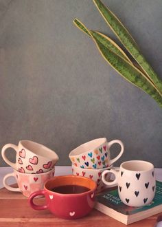 four coffee cups with hearts painted on them are sitting next to a potted plant