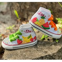 two children's shoes with fruits on them are sitting on a rock in the grass