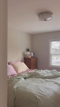 an unmade bed in a bedroom next to a window