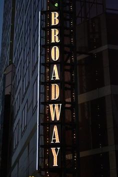 the broadway sign is lit up at night in front of a building with lights on it