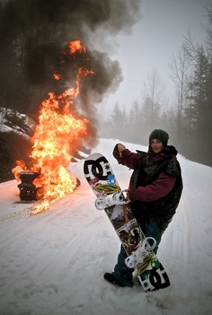 a man holding a snowboard in front of a fire