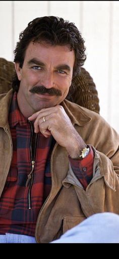 a man with a moustache sitting in a chair and looking at the camera