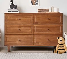 a teddy bear sitting on the floor next to a large wooden dresser in a bedroom