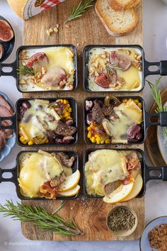 four pans filled with food sitting on top of a wooden cutting board next to bread