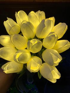 a bouquet of yellow tulips in a vase on a table with someone's hand