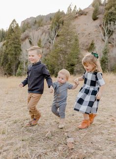 three young children are playing in the grass with their hands around each other as they walk through an open field