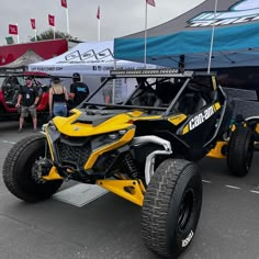 a yellow and black can - am spyster parked in a parking lot with people looking at it