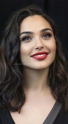 a woman with long dark hair and red lipstick smiles at the camera while wearing a black dress