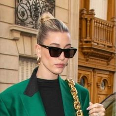 a woman with sunglasses and a green jacket is holding a gold chain in her hand