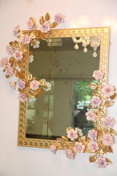 a mirror hanging on the wall with pink flowers in front of it and a gold frame