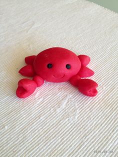 a small red crab laying on top of a white bed sheet with eyes wide open