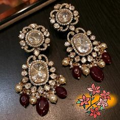 two pairs of earrings with stones and pearls on a table next to an orange flower