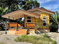 a small yellow house sitting on top of a dirt field next to trees and bushes