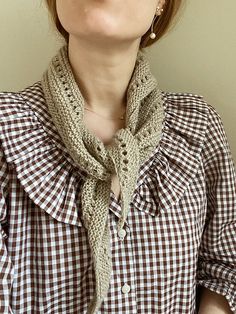 a woman wearing a brown and white checkered shirt with a scarf around her neck