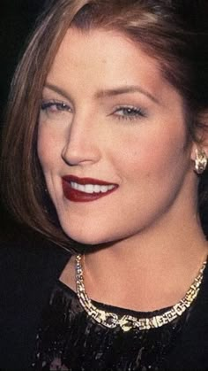 a close up of a person wearing a necklace and earrings with red lipstick on her face