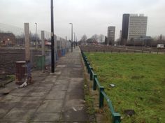 an empty street in the middle of a city with tall buildings on either side and green grass growing along both sides