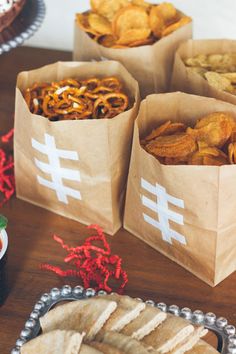 three brown paper bags filled with food on top of a wooden table next to other foods