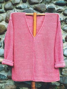 a pink cardigan sweater hanging on a wooden hanger next to some stone wall