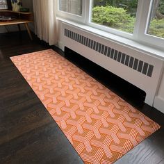 an orange and white area rug in front of a window on a hardwood floor next to a radiator