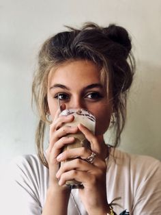 a woman drinking from a glass while wearing a white shirt