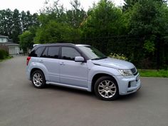 a silver suv is parked on the street in front of some bushes and trees,