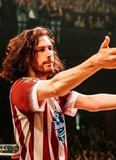 a man with long hair holding a basketball in his right hand and pointing to the side