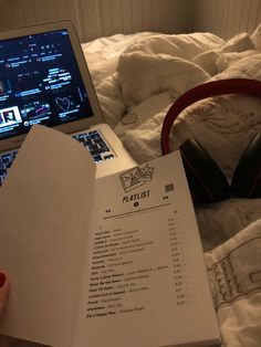 a person is reading a playlist in front of a laptop on a bed with headphones