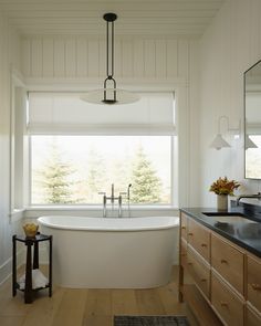 a white bath tub sitting under a window next to a wooden dresser and counter top