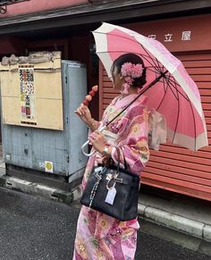 a woman in a kimono holding an umbrella on the side of the road near a building